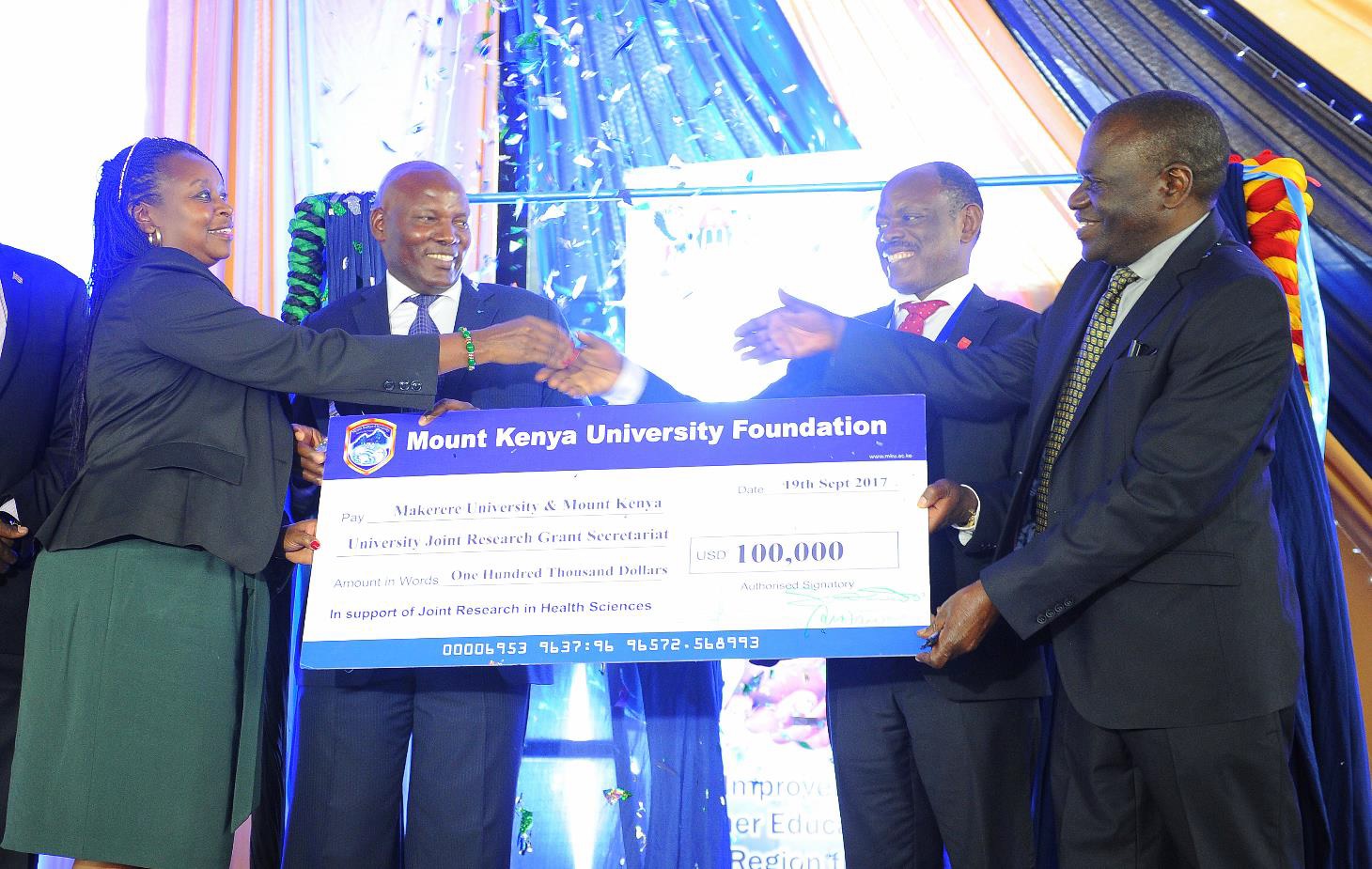 Mount Kenya University founding Vice-Chancellor Prof. Stanley Waudo {right} and Makere University Vice-Chancellor Prof. Barnabas Nawangwe { second right } receive a cheque of 10 million Kenyan shillings from MKU member Board of Directors and representative of MKU Foundation Patron, Dr. Jane Nyutu {left} and MKU Pro-Chancellor Dr. Vincent Gaitho, during the launch of MKU and Makere University College of Health Science seed grant.